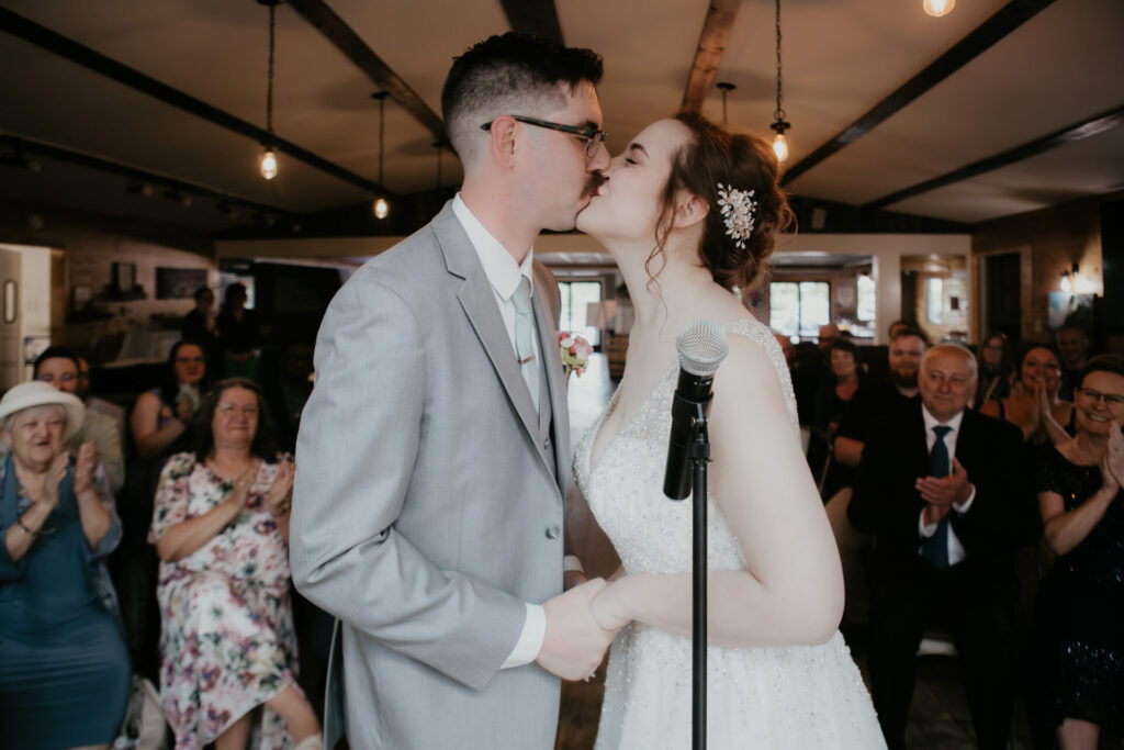Bride and groom share their first kiss at indoor wedding ceremony in Michigan, captured by Arielle Roth Photography.
