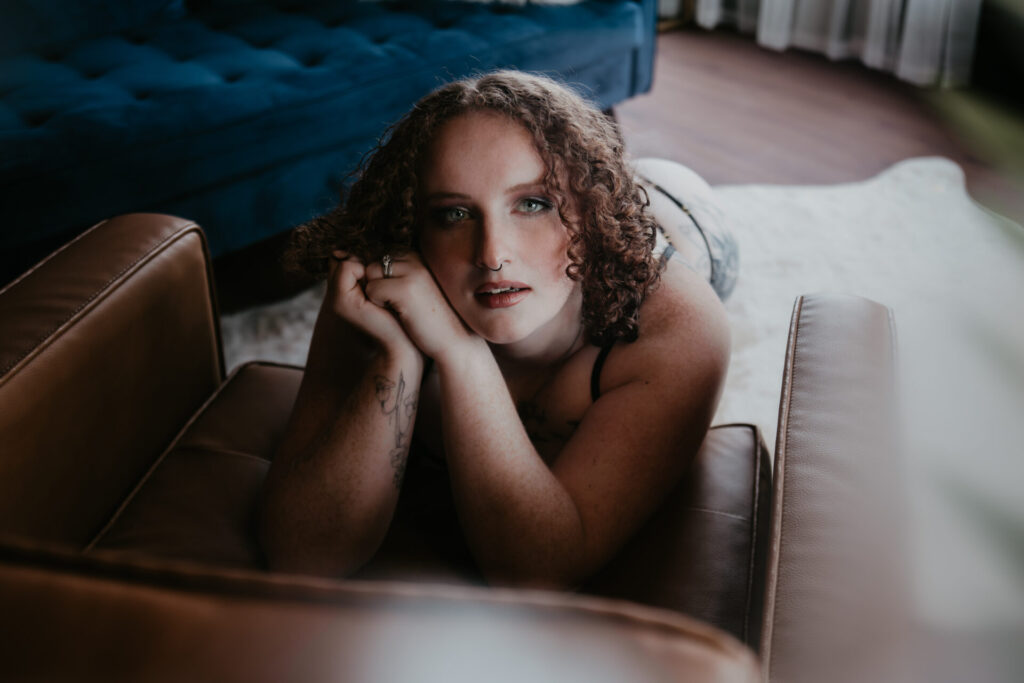 Curly-haired woman in lingerie posing confidently on a leather chair at Arielle Roth Boudoir studio