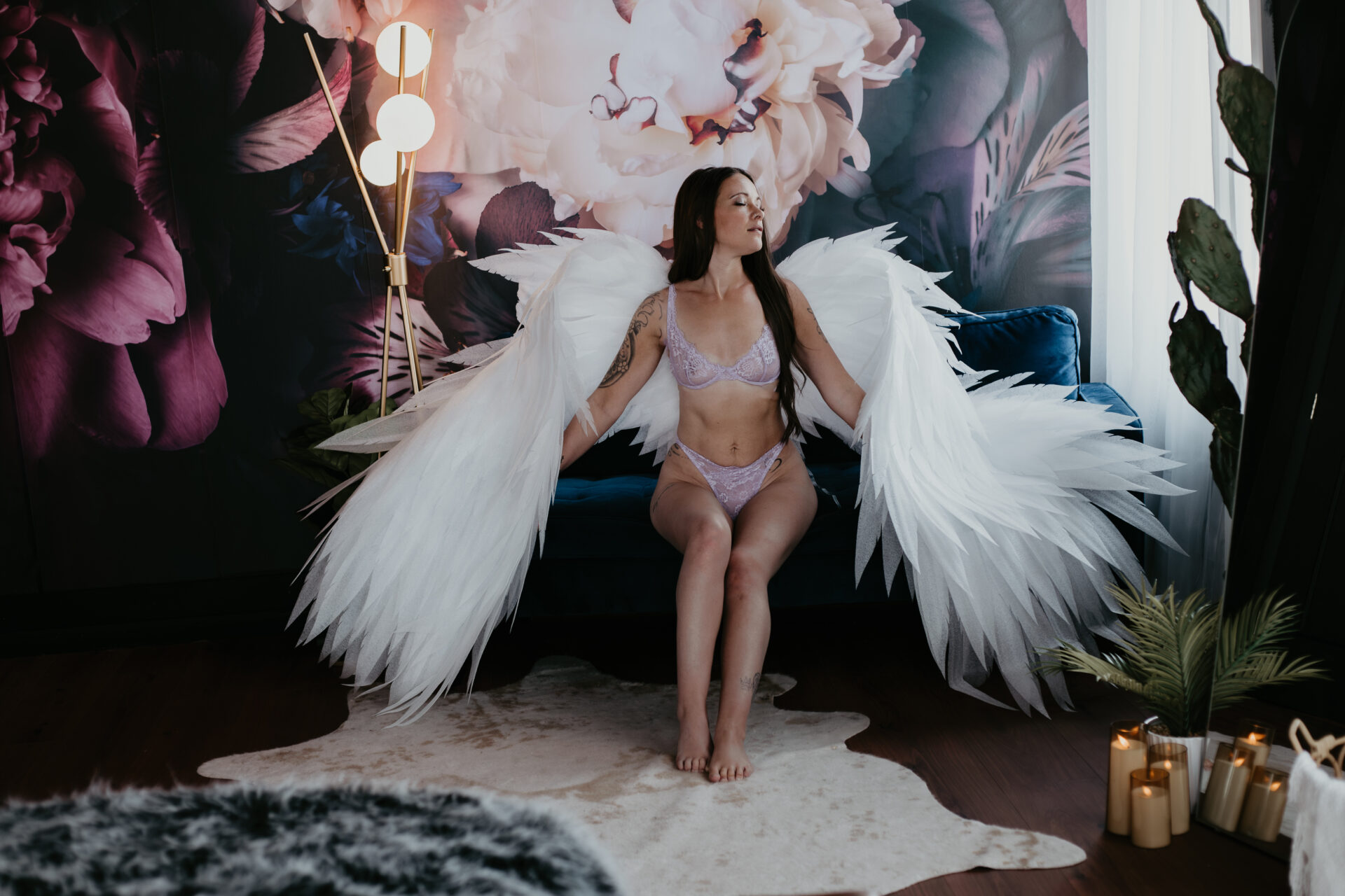 Woman in lilac lingerie wearing large white angel wings during boudoir session in Bay City, Michigan studio