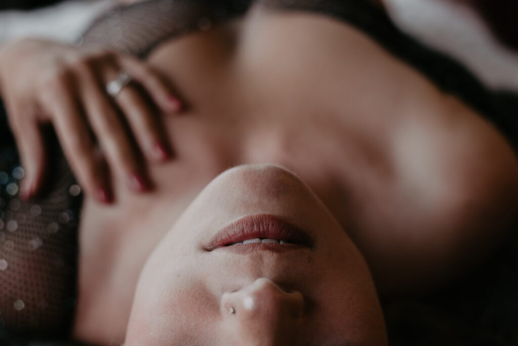 Close-up of woman’s lips and chest in a sensual boudoir pose wearing sparkly black lingerie