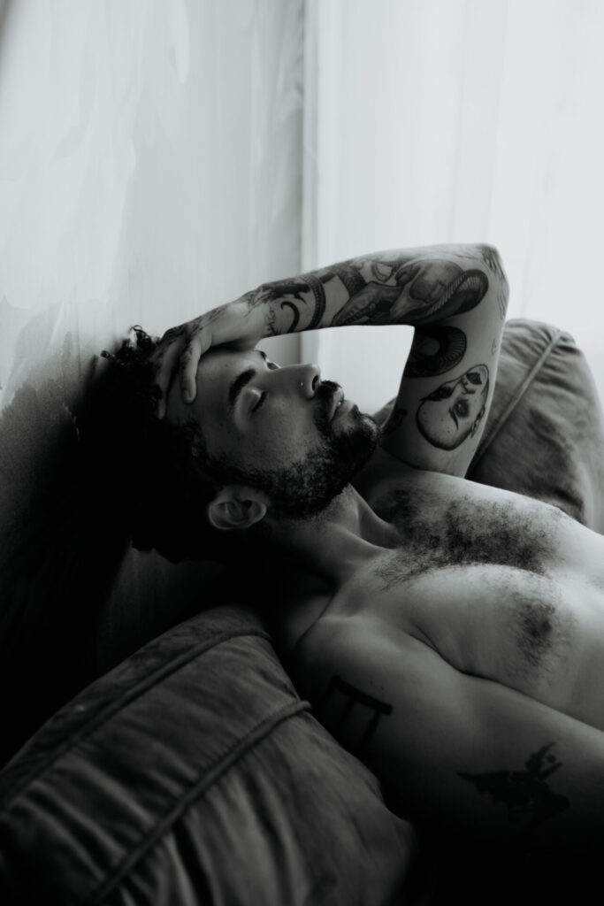 Black and white boudoir portrait of tattooed Detroit man reclining with eyes closed