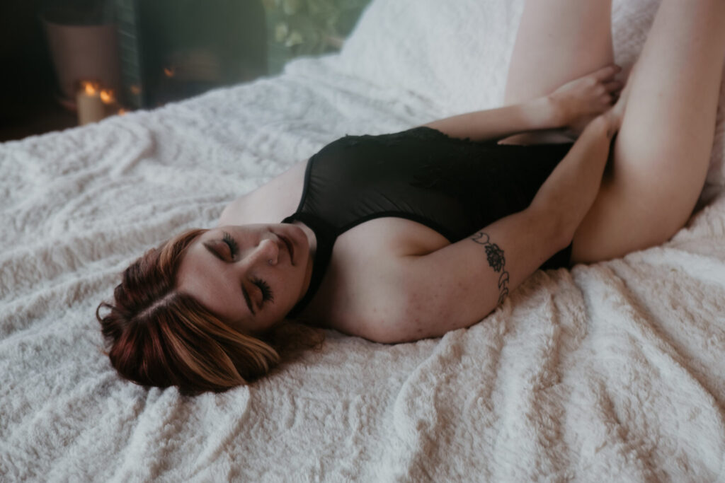 Boudoir photography in Bay City Michigan with woman in black bodysuit lying on bed