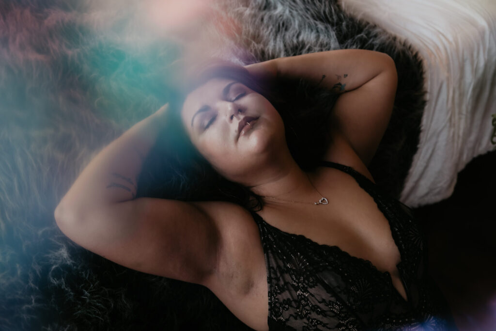 Boudoir photography in Bay City Michigan featuring a woman in black lace lingerie reclining on a fur blanket with soft dreamy light