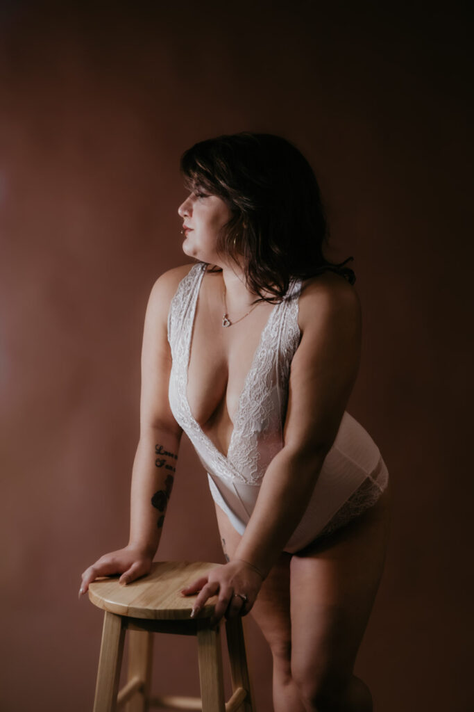 Michigan boudoir photography studio portrait in white lace bodysuit leaning on stool
