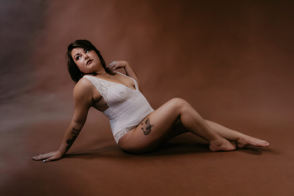 Boudoir session pose on floor in white lace bodysuit, Bay City Michigan