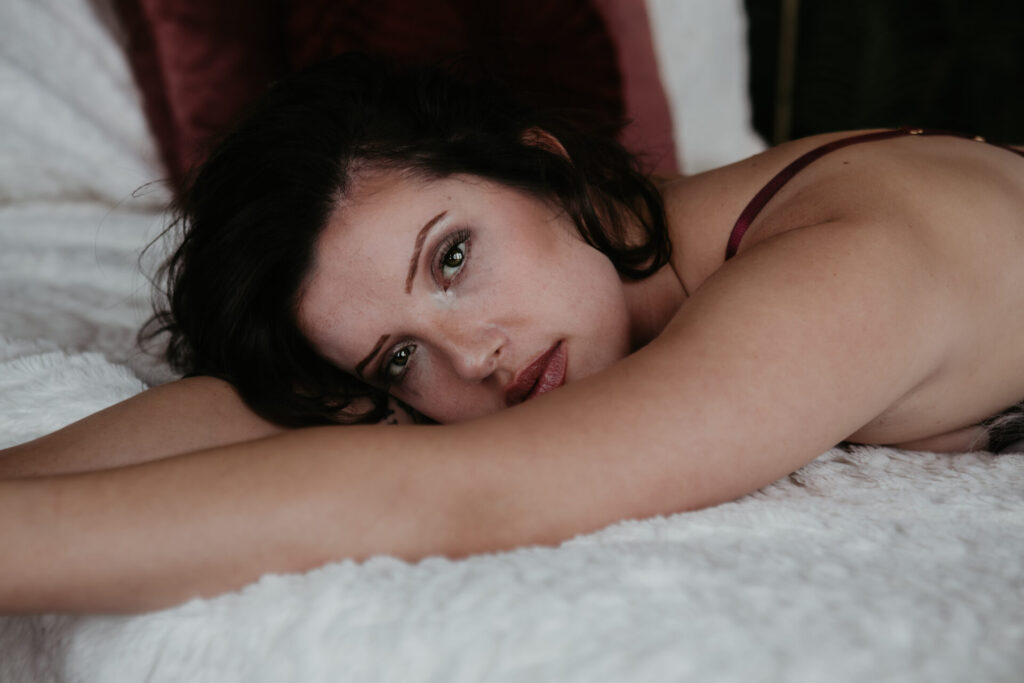 Close-up boudoir portrait of a Coleman, Michigan client in burgundy lingerie lying on a bed, photographed in my Bay City boudoir studio.