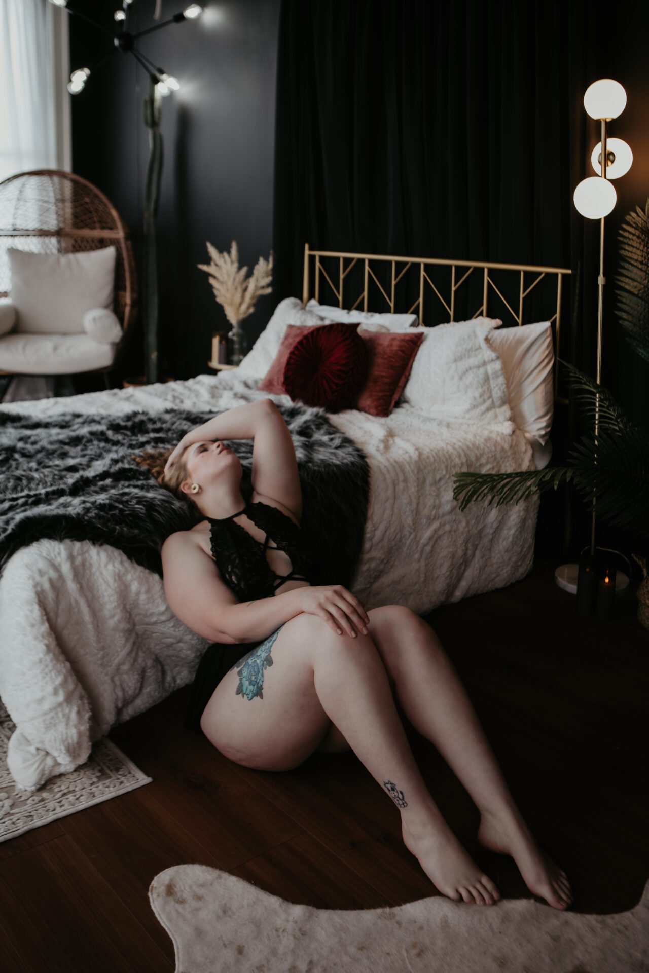 Boudoir photo of a Saginaw client in black lace lingerie sitting on the floor by the bed at Arielle Roth Boudoir studio in Bay City, Michigan