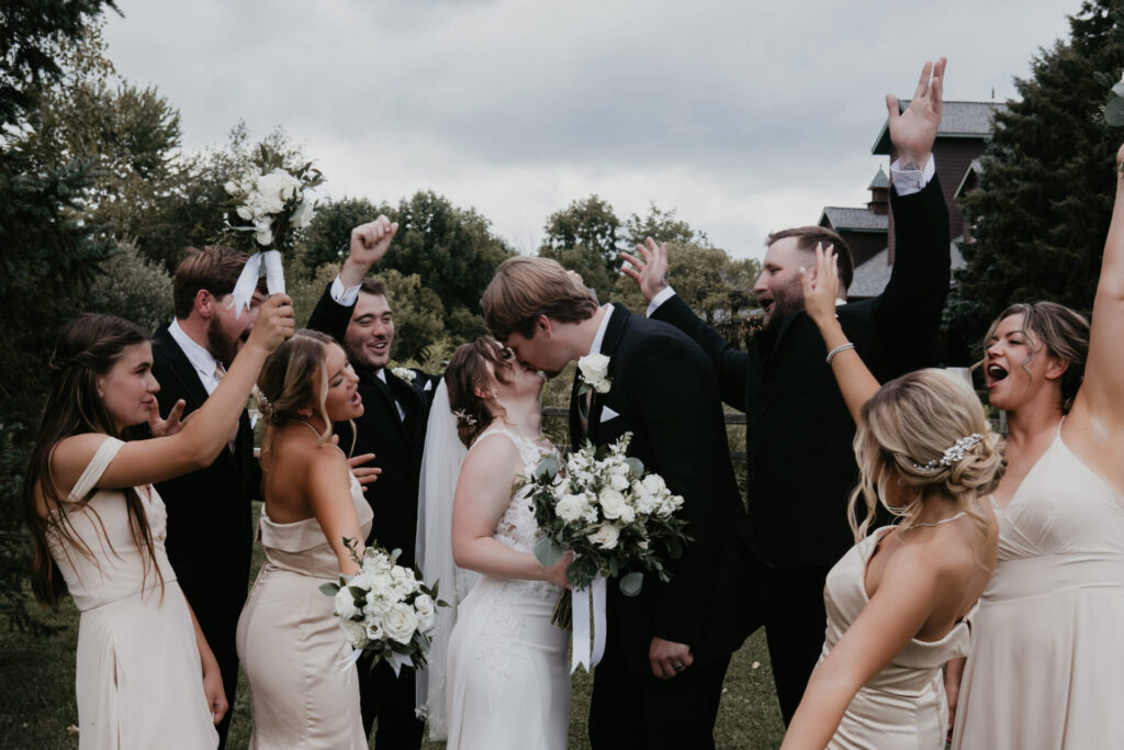 Bride and groom kiss surrounded by cheering wedding party at Michigan celebration