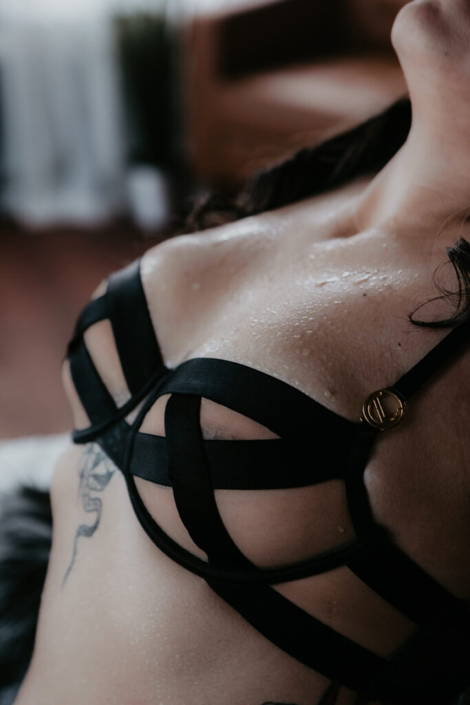 West Branch Michigan boudoir client’s upper body in a black strappy bra with water droplets glistening on her skin, photographed by Arielle Roth Boudoir.