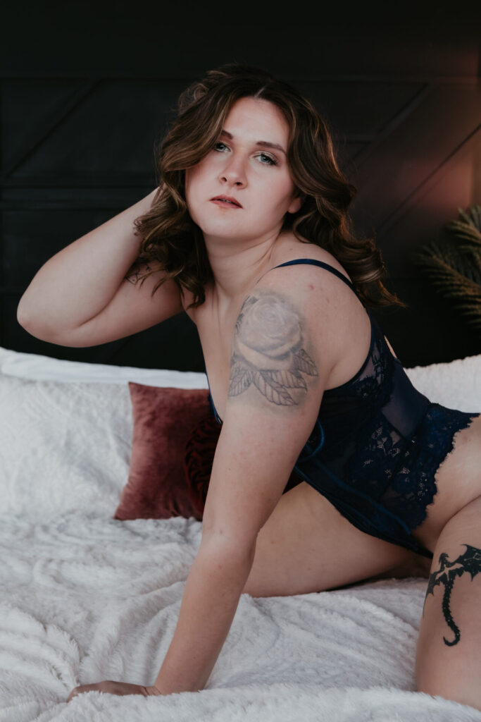 Boudoir portrait of a woman from Chesaning kneeling on a bed in navy lace lingerie with her hand in her hair during a session in Bay City Michigan