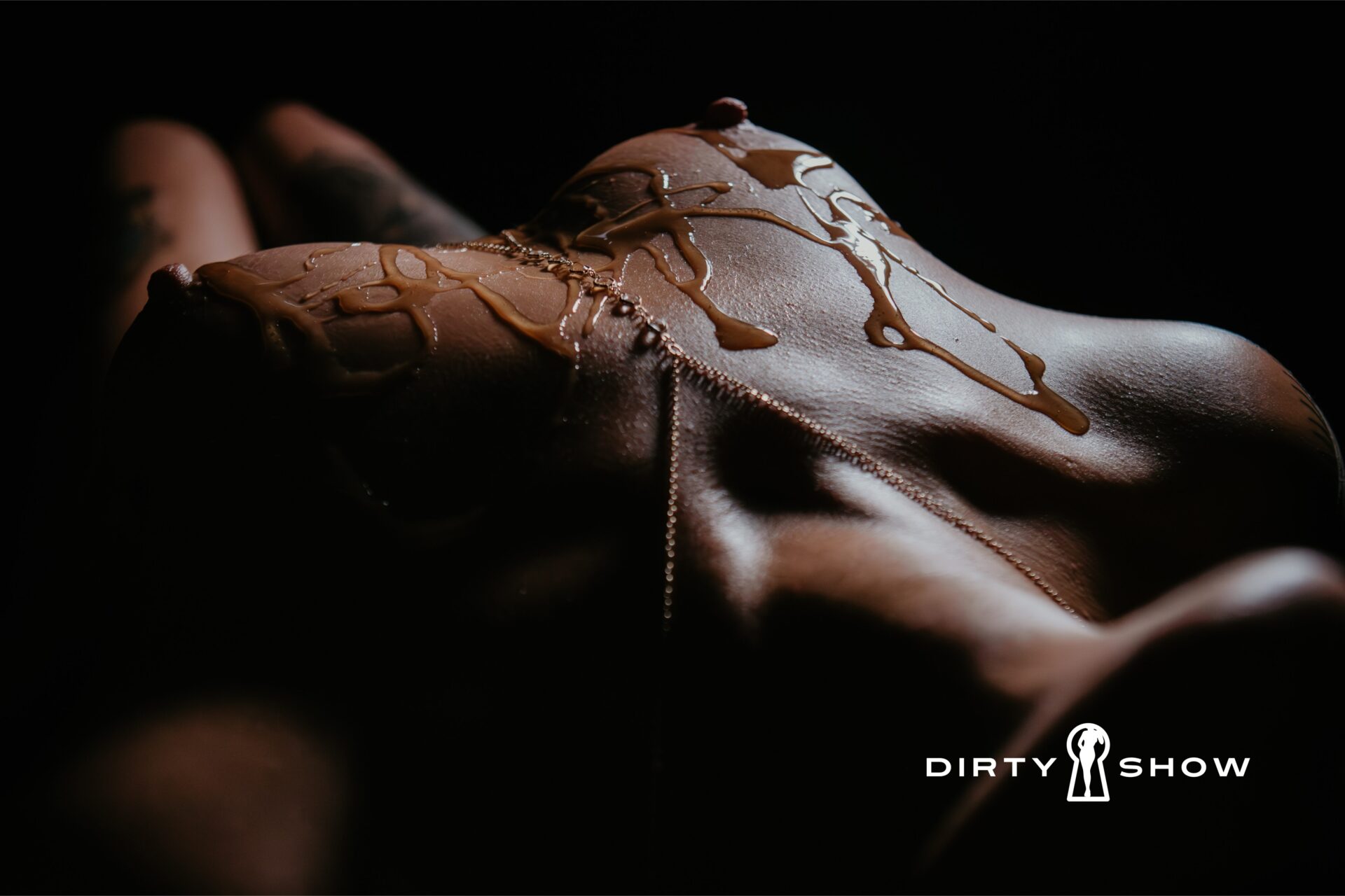 Fine art boudoir photograph of a reclined torso with honey dripped across the body in dramatic low light, featuring The Dirty Show logo, created by a Bay City, Michigan boudoir photographer.