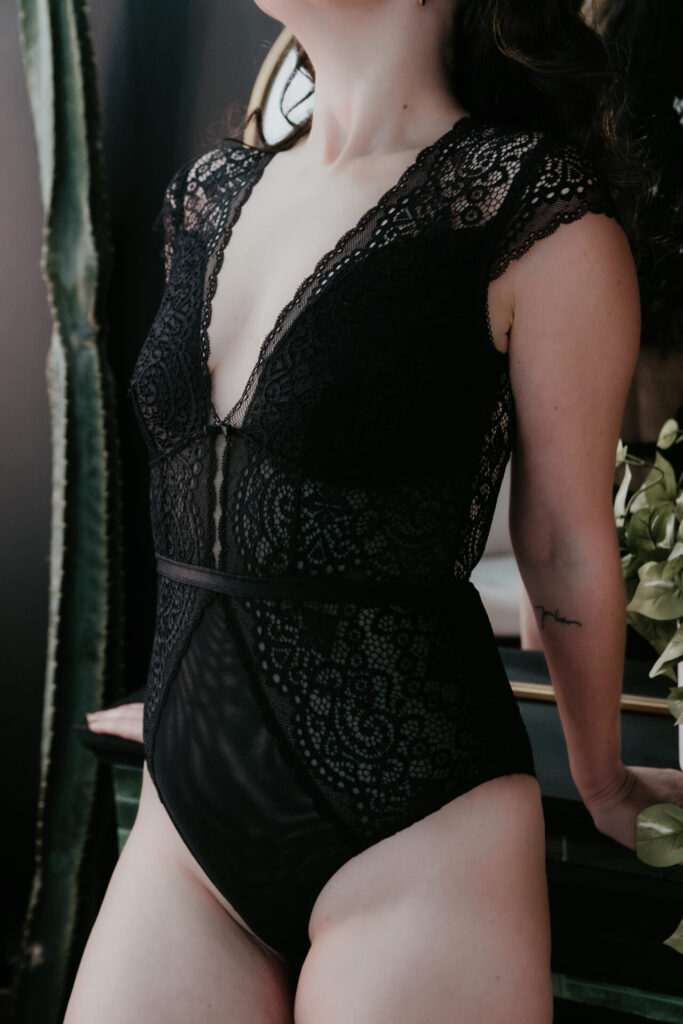 Plus size boudoir portrait of a woman wearing a black lace bodysuit, photographed in a Bay City Michigan boudoir studio by Arielle Roth Boudoir