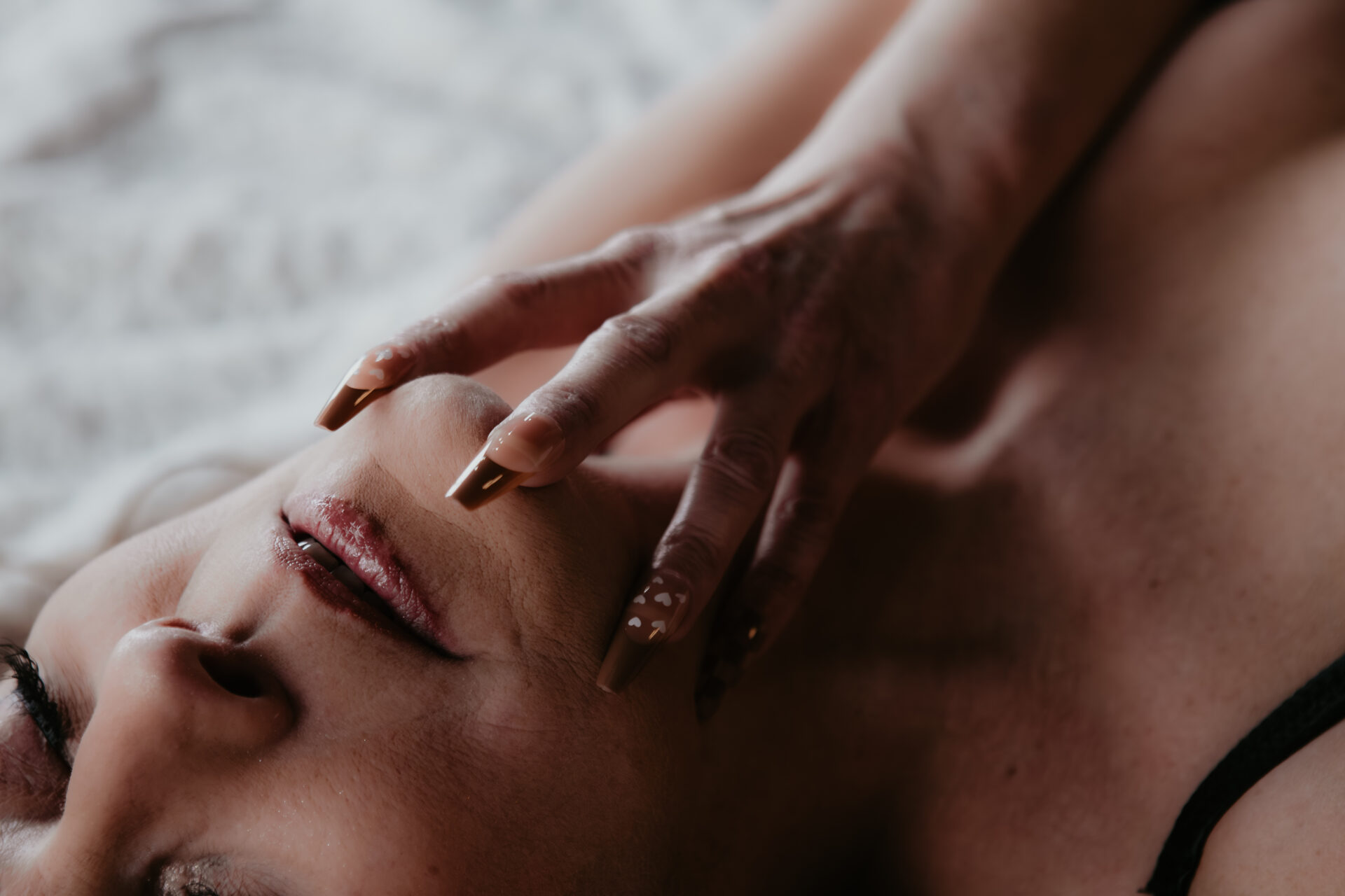 Close-up boudoir portrait of a mature woman lying back with fingers resting near her lips, photographed in natural light at a Michigan boudoir studio.