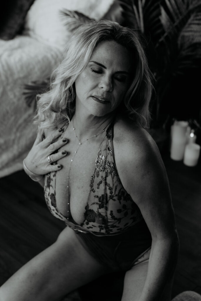 Mature woman seated in a lace bodysuit during a black and white boudoir session, photographed by a Bay City Michigan boudoir photographer, client from Traverse City