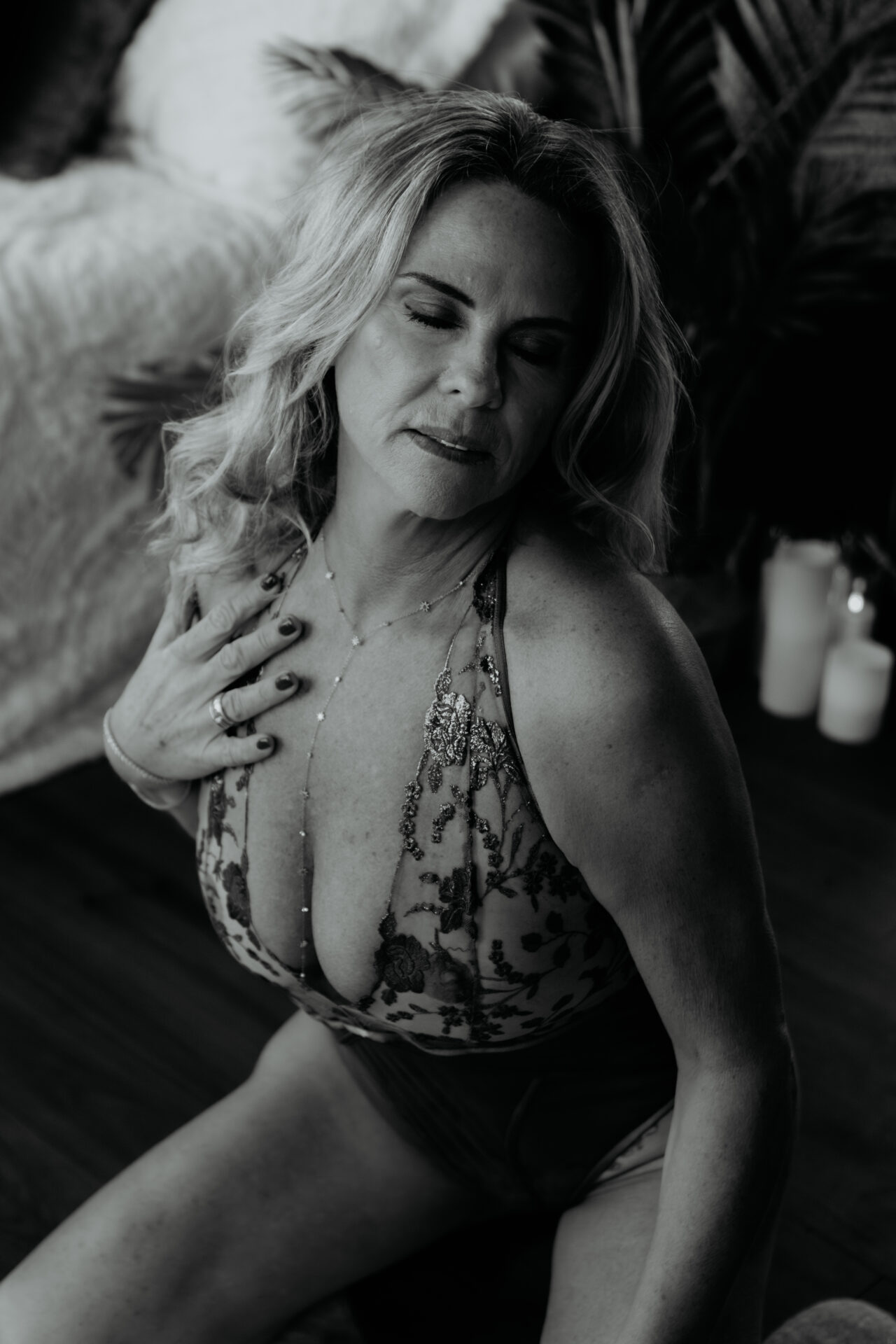 Mature woman seated in a lace bodysuit during a black and white boudoir session, photographed by a Bay City Michigan boudoir photographer, client from Traverse City