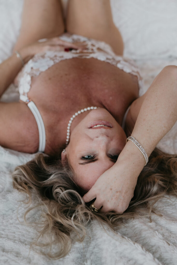 Mature woman lying on a bed with relaxed eye contact during a boudoir session, photographed by a Bay City Michigan boudoir photographer, client from Traverse City