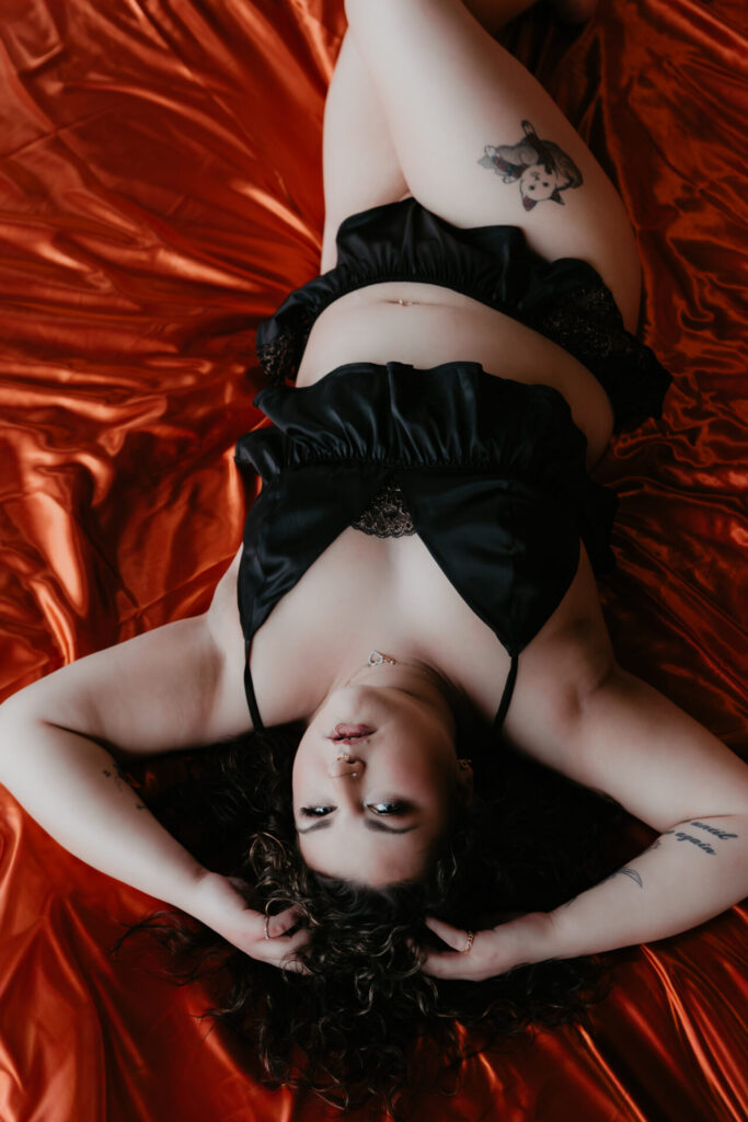 Close-up boudoir portrait of a client laying on red satin sheets in black lingerie during a dramatic studio boudoir session with Arielle Roth Boudoir in Bay City, Michigan.
