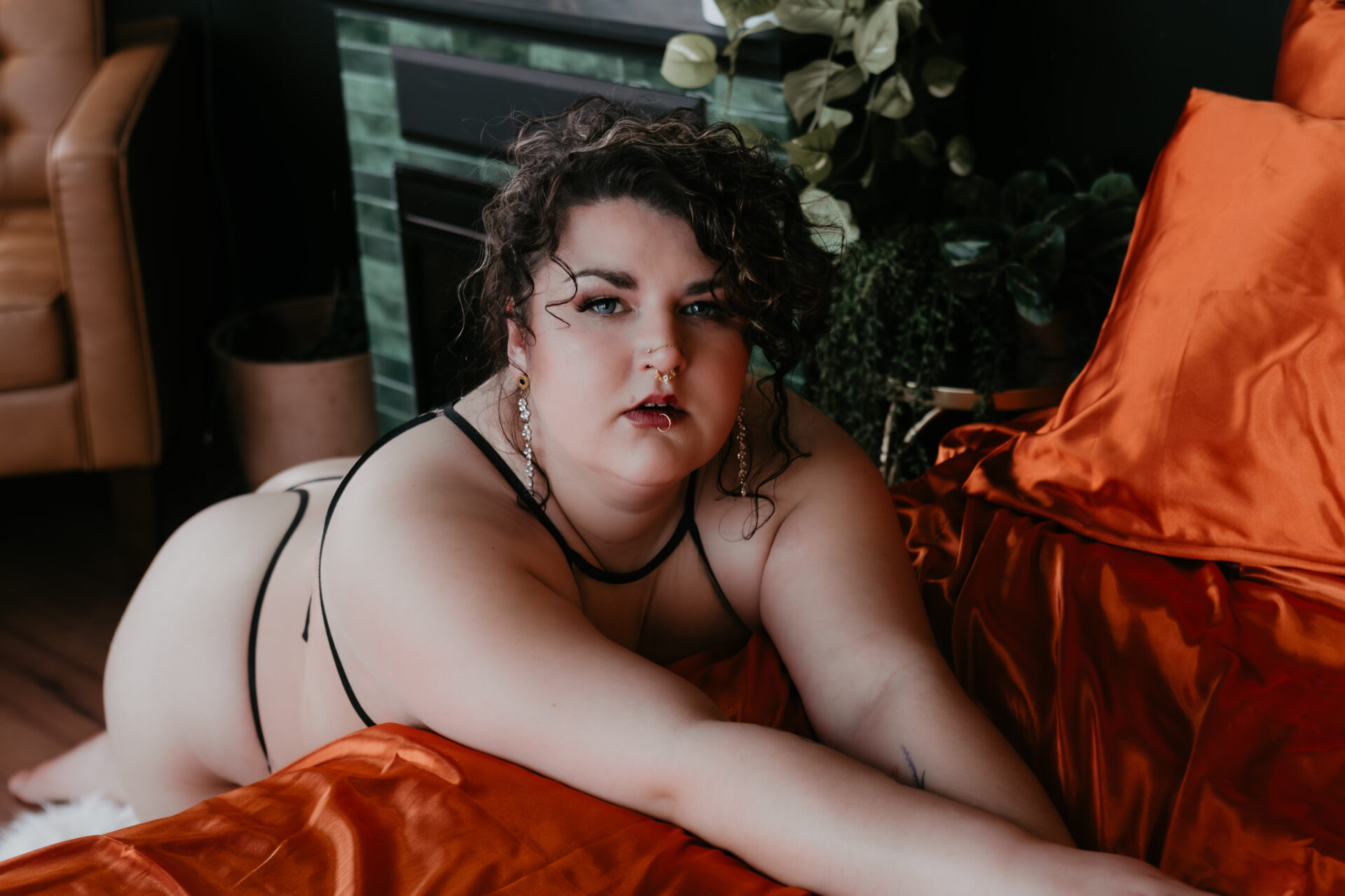 Boudoir portrait of a client in black strappy lingerie posing on red satin bedding in a Bay City Michigan boudoir studio.